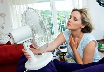 A woman uses a small white fan to cool her face, eyes closed in relief from the heat.