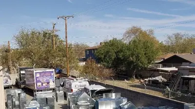 An outdoor lot displays stacks of silver HVAC ductwork and service trucks. Photo