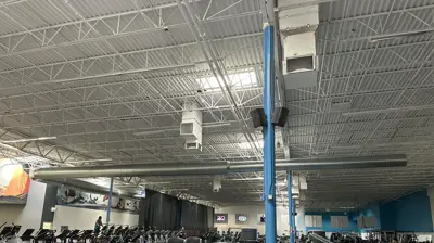 A fitness center with cardio and weight machines under exposed white ceiling trusses. Photo