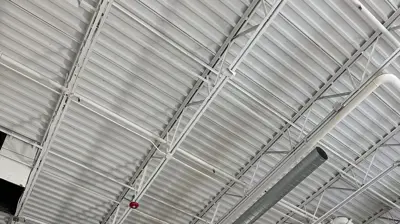 An indoor space under construction features an exposed white ceiling with metal decking and trusses. Photo