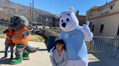 A young girl stands smiling between a white polar bear mascot and a gray wolf mascot. Photo