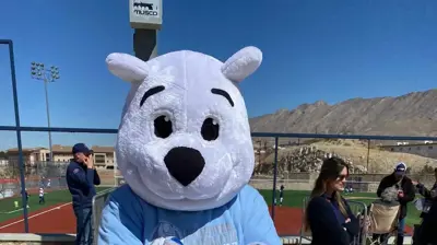 A friendly white bear mascot in a light blue shirt holds small blue and white items. Photo