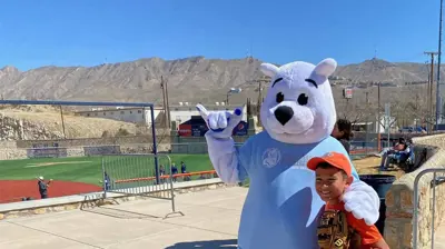 A friendly polar bear mascot in a light blue shirt stands beside a smiling boy wearing a baseball glove. Photo