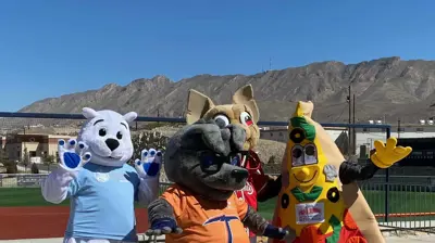 Three mascots stand on a field with mountains in the background. Photo