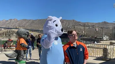 A white polar bear mascot waves next to a young man in a blue and orange jacket. Photo