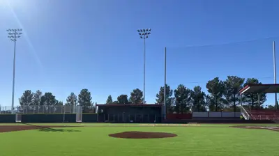 A bright, clear view of an empty baseball field with green artificial turf and a dirt pitcher's mound. Photo