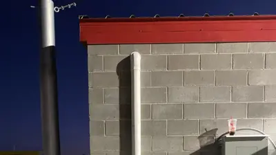 An outdoor Fujitsu HVAC unit, part of a Multi Zone VRV System, is mounted on a gray brick wall with a pipe extending upwards. Photo
