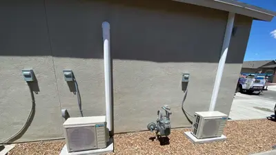 An exterior view of a building. Two mini-split AC units and a gas meter are installed. Photo
